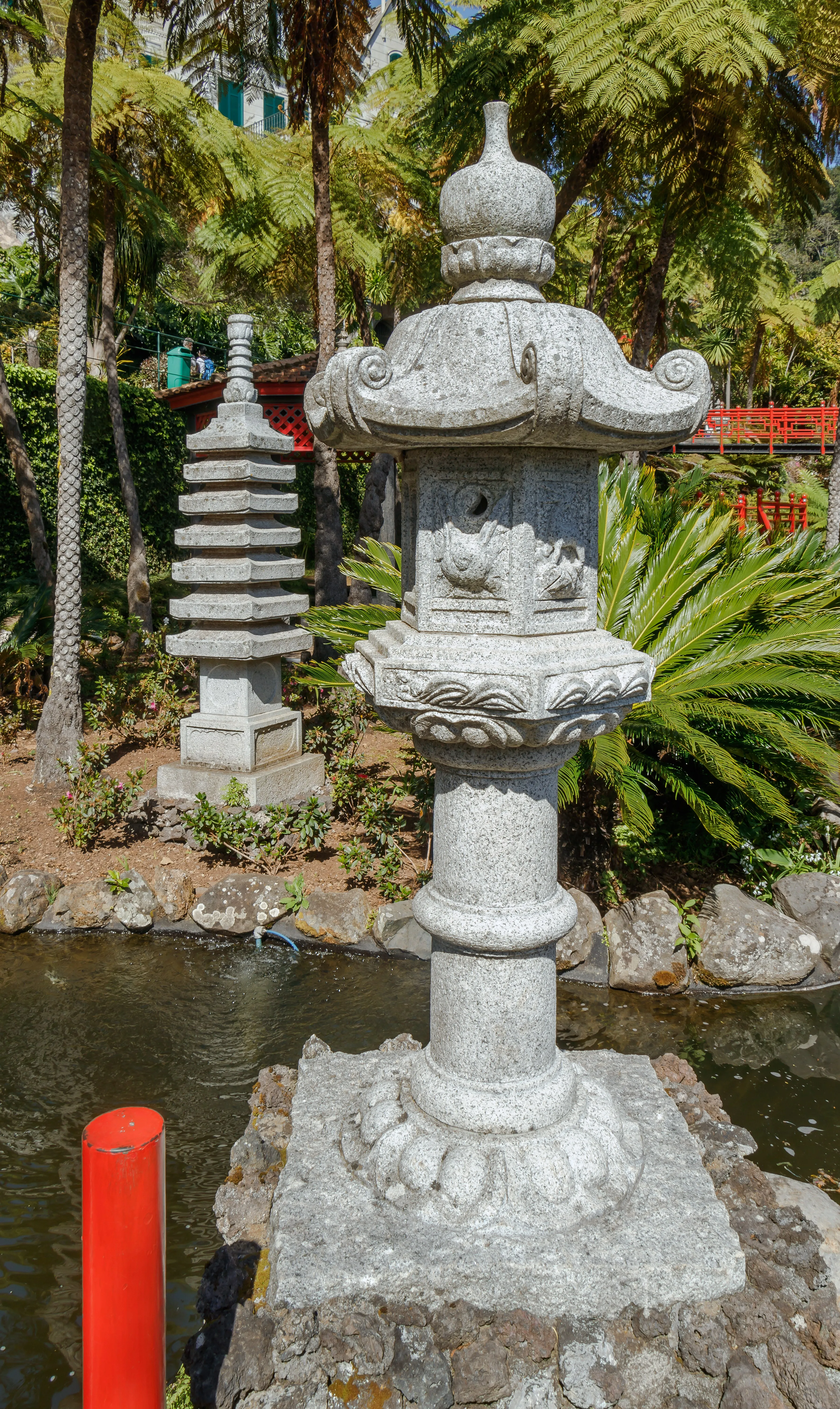Shaded garden with a stone bridge over water, framed by ferns and palms